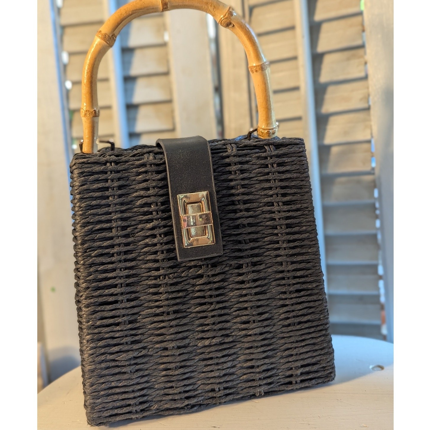 Black woven handbag with bamboo handle and gold chain strap