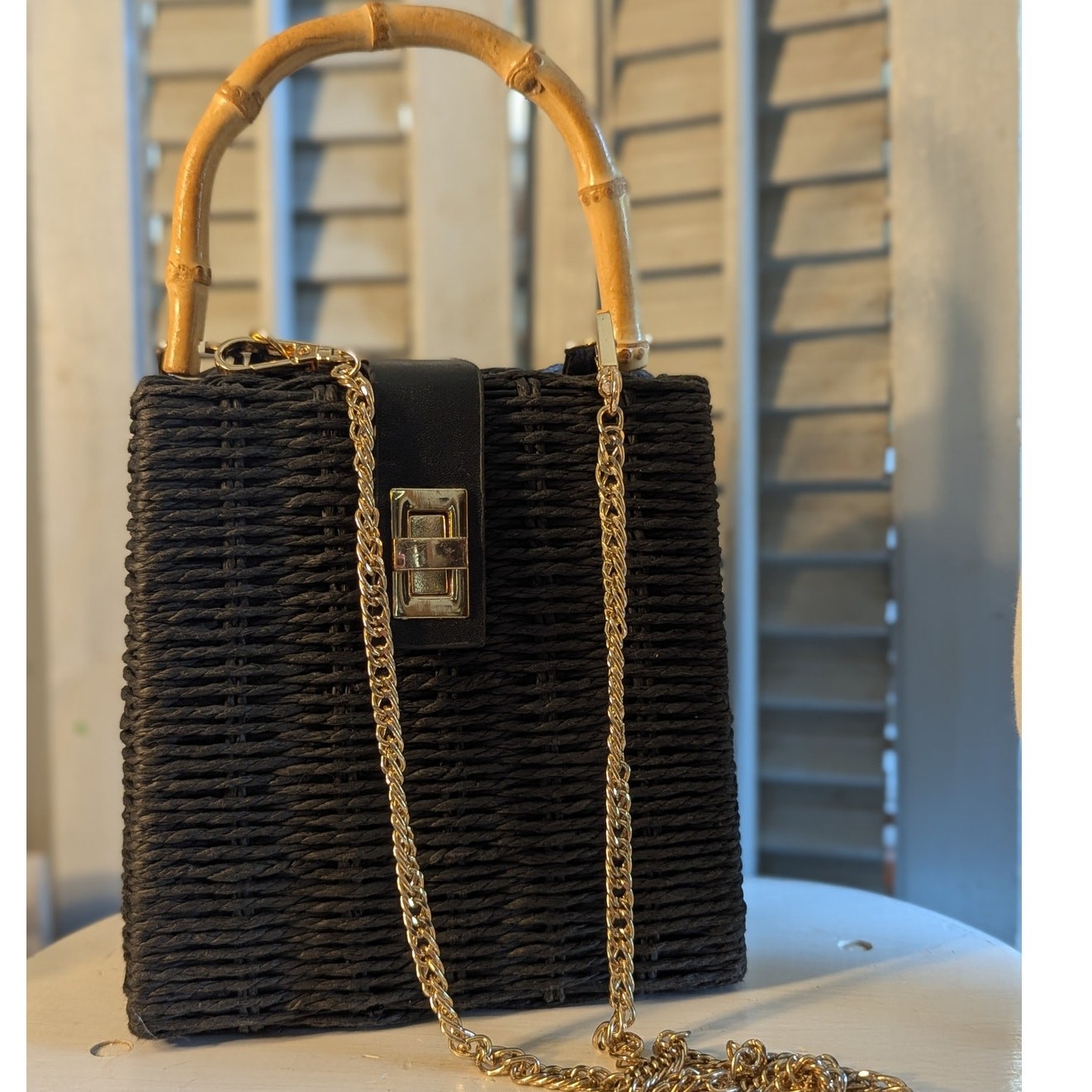 Black woven handbag with bamboo handle and gold chain strap